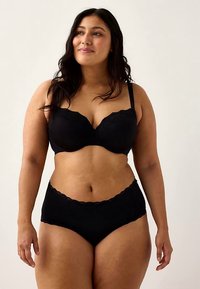 Svart behå med spetskant och högmidjade trosor, med slät tyg och justerbara band, visade på en modell mot en neutral bakgrund.