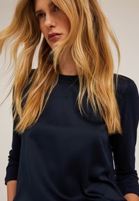 Maglietta a maniche lunghe blu navy con una texture liscia e setosa e un sottile accento glitterato sul collo. Vestibilità sagomata, tessuto leggero.