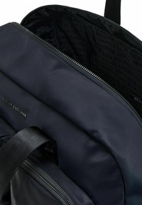 Zaino in nylon nero con apertura con zip, dotato di una fodera interna con un motivo ripetuto "Armani Exchange" e una tracolla resistente.
