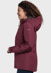 Burgundowa wodoodporna kurtka z wysokim kołnierzem, regulowanym kapturem i zamykanymi na zamek kieszeniami. Gładka struktura i luźny krój, odpowiednia do użytku na świeżym powietrzu.