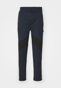 Mörkblå byxor med dragsko i midjan, med kontrasterande svarta och grå paneler, rak bendesign, slät struktur och sidofickor.