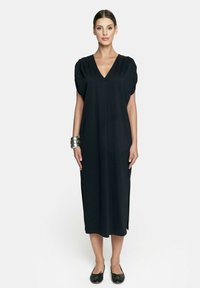 Czarna midi sukienka z dekoltem w kształcie litery V i krótkimi rękawami. Miękka tkanina z rozporkami po bokach. Płaskie czarne buty i srebrna bransoleta na nadgarstek.