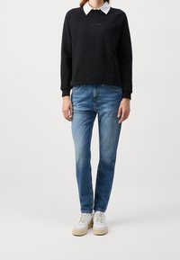 Czarna bluza z białym kołnierzykiem, zestawiona z niebieskimi dżinsami i białymi sneakersami o jasnej podeszwie. Prosty, casualowy strój.