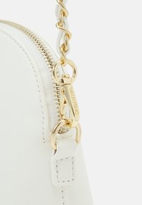 Vit läderväska med guld-detalk, med dragkedjestängning och en flätad kedjeslinga. Anmärkningsvärd sömdetalj förstärker designen.