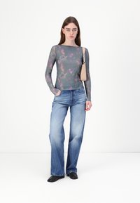 Long-sleeve top in sheer gray fabric with purple floral patterns, paired with light blue flared jeans and black shoes. Small beige handbag.