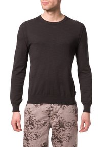 Suéter negro de manga larga tejido, con cuello redondo, puños acanalados y dobladillo ajustado, llevado sobre pantalones claros con patrón.