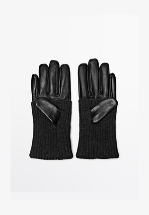 Gants en cuir noir avec poignets en tricot côtelé, présentant une texture lisse et un design à cinq doigts. Accents en matériau contrastant au niveau du poignet.