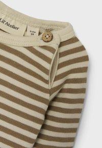 Top a maniche lunghe a righe beige e marrone realizzato in morbido cotone. Presenta un bottone di legno sulla spalla e un colletto arrotondato.