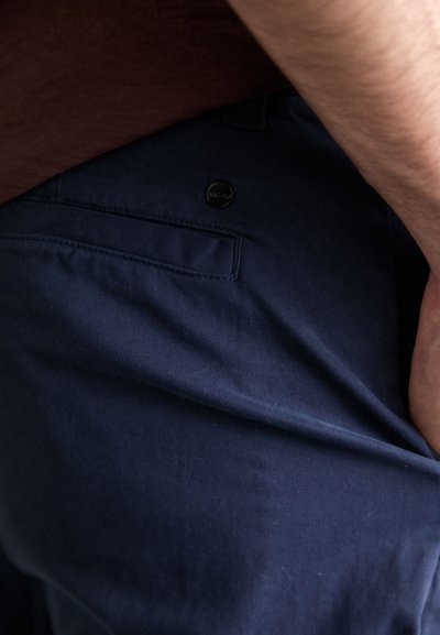 Pantalons en coton bleu marine avec une texture lisse, dotés d'une poche arrière et d'un petit bouton logo circulaire à la taille.