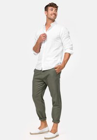 Chemise blanche en lin à boutons, pantalon vert et chaussures légères. Les pantalons sont retroussés aux chevilles. Texture lisse avec un design décontracté.