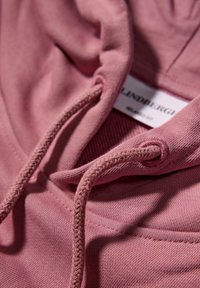 Tejido de sudadera rosa con una textura suave, que presenta un cordón. La etiqueta visible dice "LINDBERGH" y "CORTE RELAJADO."