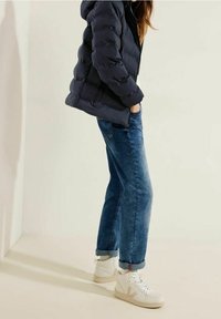 Granatowa kurtka puchowa, niebieskie podwinięte dżinsy i białe buty sportowe z beżowymi akcentami. Gładkie materiały i klasyczny, casualowy design.