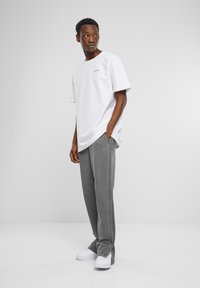 T-shirt en coton blanc avec un logo rose, associé à un pantalon en velours côtelé gris. Le modèle porte des baskets blanches, se tenant sur un fond uni.