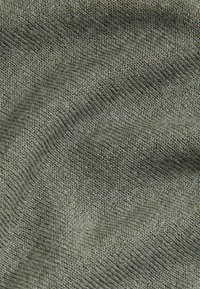 Tissu texturé vert olive avec un motif de tricot fin, présentant une surface douce et lisse ainsi que des variations subtiles de teinte.