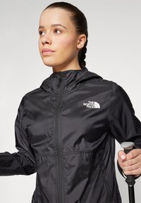 Schwarze leichte Jacke mit Reißverschluss vorne und Kapuze. Verfügt über ein Logo auf der oberen linken Brust und einen strukturierten Stoff. Geeignet für den Außeneinsatz.