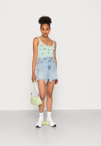Top cropped azul claro com bordados florais, combinado com uma saia mini em denim desfiada, bolsa verde e ténis brancos com detalhes amarelos.