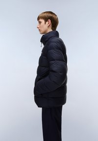 Marineblå jakke i puffer-stil med høj krave, quiltet design og lynlås foran. Har sidelommer og en glat, blank tekstur.