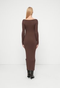 Brun ribbestrikket kjole med lange ermer og vid hals, tettsittende silhuett, som rekker til midt på leggen, kombinert med svarte knelange støvler.