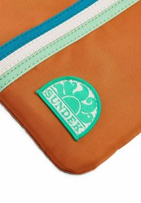 Borsa di tessuto arancione con strisce turchesi, verde menta e bianche, con un logo circolare verde "SUNDEK" e cuciture testurizzate.