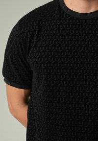 Camiseta negra de manga corta con un patrón texturizado de formas geométricas, con un cuello acanalado y tejido suave.