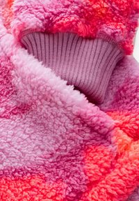 Lähivaade roosast ja punasest kohevast fliiskangast koos helelilla soonikkoega varrukapikendusega.