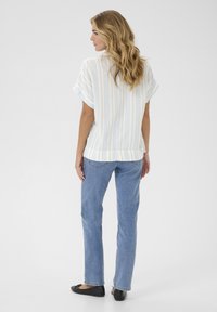 Striped short-sleeve top in light yellow and blue; loose fit with a rounded hem, paired with blue straight-leg jeans and black flats.