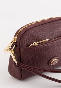 Wine-colored synthetic leather bag with gold hardware, featuring a zip closure, textured surface, and a round accent detail.