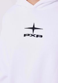 Sudadera blanca con un logotipo bordado en negro que presenta una estrella y el texto "PXP" debajo. La tela parece suave y lisa.