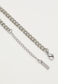 Silberner Metallkettenaccessoire mit ineinandergreifenden Gliedern, einem Karabinerhaken und einer Verlängerungskette mit einem kleinen Anhängerdetail.