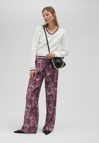 White sweater with a V-neck and striped hem, paired with pink leopard print wide-leg pants. Black textured handbag and pointed shoes featured.