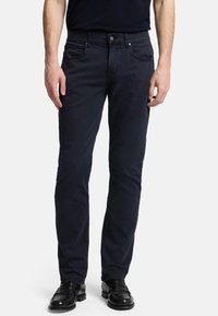 Pantaloni in cotone blu navy con vestibilità slim, design a cinque tasche, chiusura con bottone e dettagli di cucitura sottili. Indossati con scarpe in pelle nere.