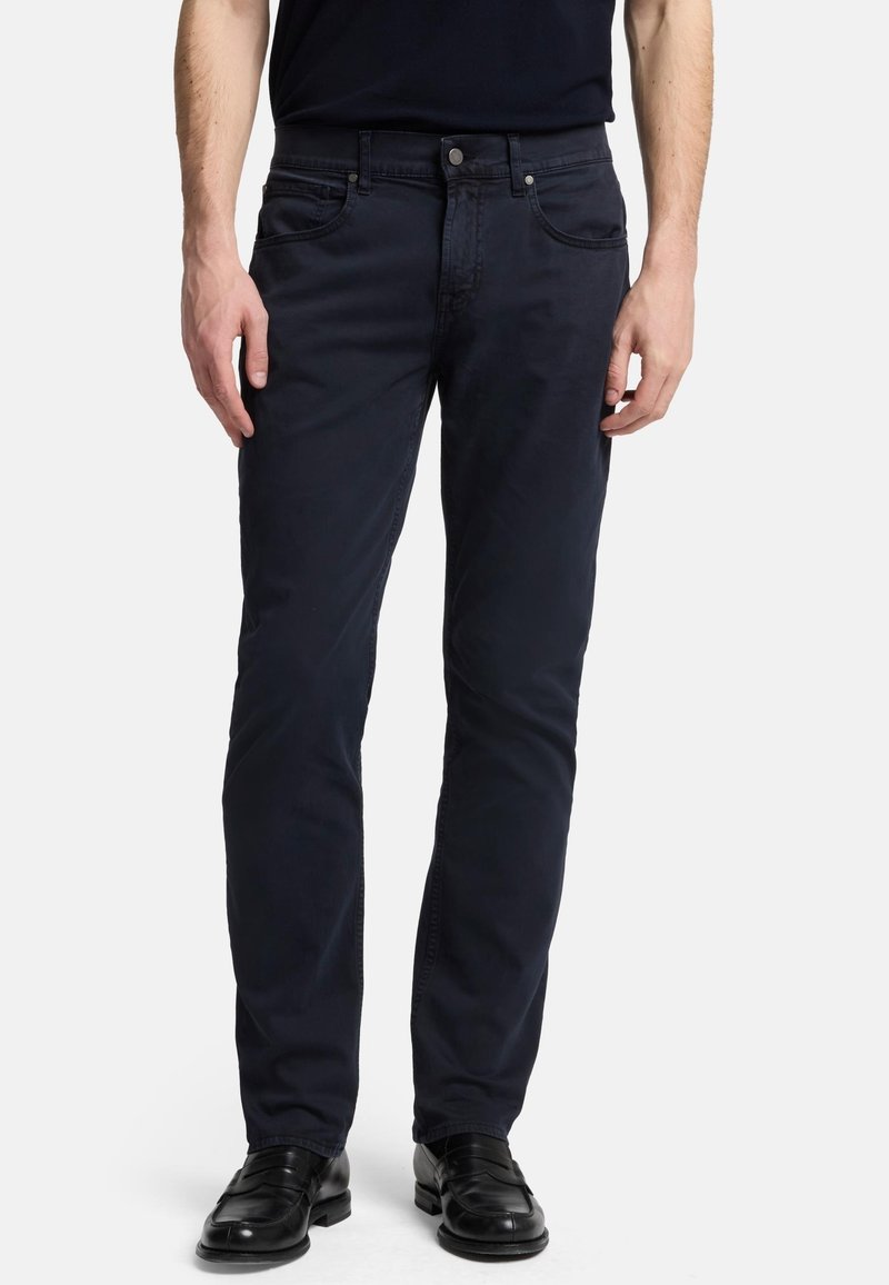 Pantaloni in cotone blu navy con vestibilità slim, design a cinque tasche, chiusura con bottone e dettagli di cucitura sottili. Indossati con scarpe in pelle nere.