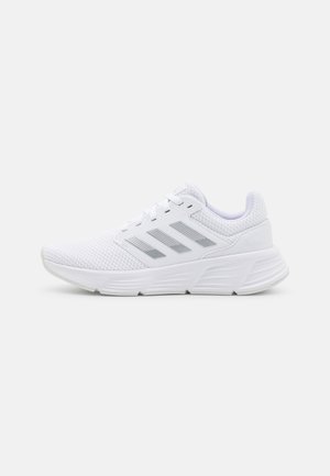 White athletic shoes made of mesh material, featuring three silver stripes, a textured sole, and a padded collar for comfort.