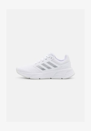 White athletic shoes made of mesh material, featuring three silver stripes, a textured sole, and a padded collar for comfort.