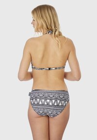 Bikini noir et blanc avec des motifs géométriques. Décolleté halter avec un fermoir dans le dos et un bas de maillot texturé.