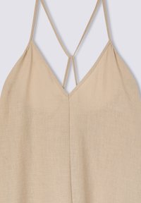 Top in lino beige con scollatura a V e spalline sottili che formano un design incrociato nella parte posteriore. Texture liscia con dettagli minimi.