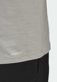 Ljusgrå idrottströja med en slät textur, rundad sömn, och AEROREADY-logotypen nära botten, i kombination med svarta shorts.