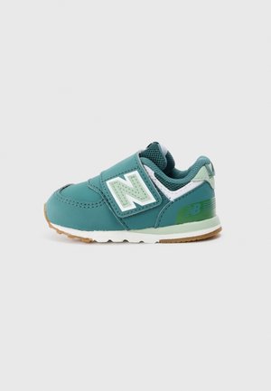 Zapatilla New Balance para niño pequeño en colores verde azulado y verde, con cuello de malla, cierre de velcro y suela de goma blanca sobre un fondo gris claro.
