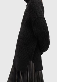 Pull noir en tricot avec un motif en losanges texturé, fente latérale à l'ourlet et coupe décontractée, associé à une jupe plissée noire.