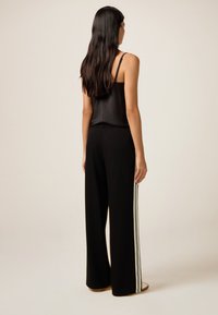 Pantalons larges noirs avec des rayures blanches sur les côtés, en tissu lisse, avec une taille élastique et une coupe décontractée.