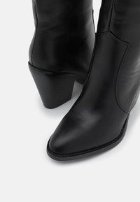 Černé kožené kotníkové boty s špičatou špičkou a texturovaným podpatkem. Mají hladký povrch a minimální švy.
