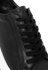 Baskets en cuir noir avec un dessus lisse, une pointe ronde, des lacets noirs et une semelle en caoutchouc blanche avec des coutures latérales.