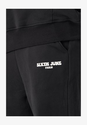 Pantaloni della tuta neri con vita a coste, tasche laterali e un logo bianco recante la scritta "SIXTH JUNE PARIS" sulla coscia sinistra.
