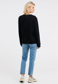 Zwarte sweatshirt met lange mouwen en ronde hals, gecombineerd met lichtblauwe jeans en beige sneakers. Minimalistisch ontwerp, gladde textuur.
