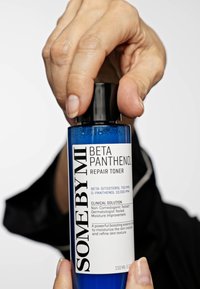 Blå sylinderformet flaske med SOME BY MI Beta Panthenol Repair Toner, med svart lokk og hvit etikett som viser produktdetaljer og instruksjoner.