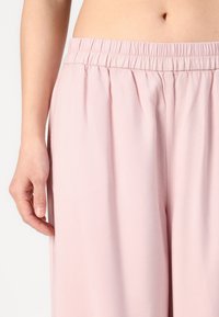 Pantaloni elasticizzati rosa chiaro con una vestibilità rilassata, realizzati in tessuto morbido e dotati di pieghe sottili per flessibilità e comfort.