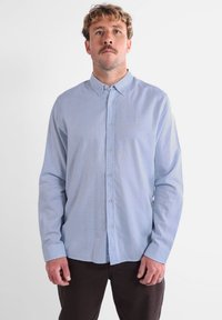 Chemise bouton de couleur bleu clair en tissu doux, dotée d'un col, de manches longues et d'un logo brodé unique sur la poitrine.