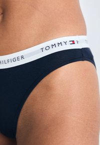 Boxers navy blue de Tommy Hilfiger avec une ceinture élastique blanche portant le nom de la marque. Tissu lisse avec une coupe ajustée.