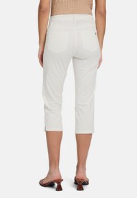 Pantalons capri blancs avec une texture lisse, taille mi-haute et deux poches arrière. Associés à des sandales à talons bruns et un haut texturé.