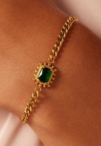 Bracelet en chaîne dorée avec une pierre verte rectangulaire sertie dans un sertissage orné. Les maillons en métal texturé créent un design contrastant.